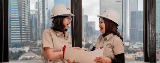 Two women in hard hats discussing construction blueprints at a job site