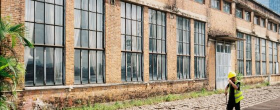 Man standing in front of a tall brick building evaluating whether to develop or renovate