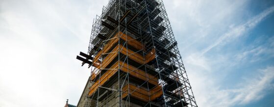 Church steeple wrapped in scaffolding during renovation against a pale sky