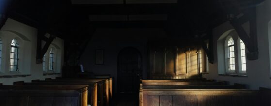 Empty wooden church pews lit by sunlight streaming through tall windows