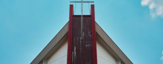 Modern church gable with a red steel cross against blue sky