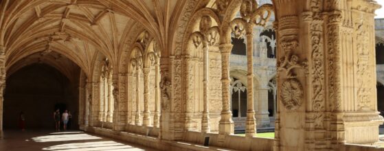 Long arched stone hallway with columns and warm light in a monastery