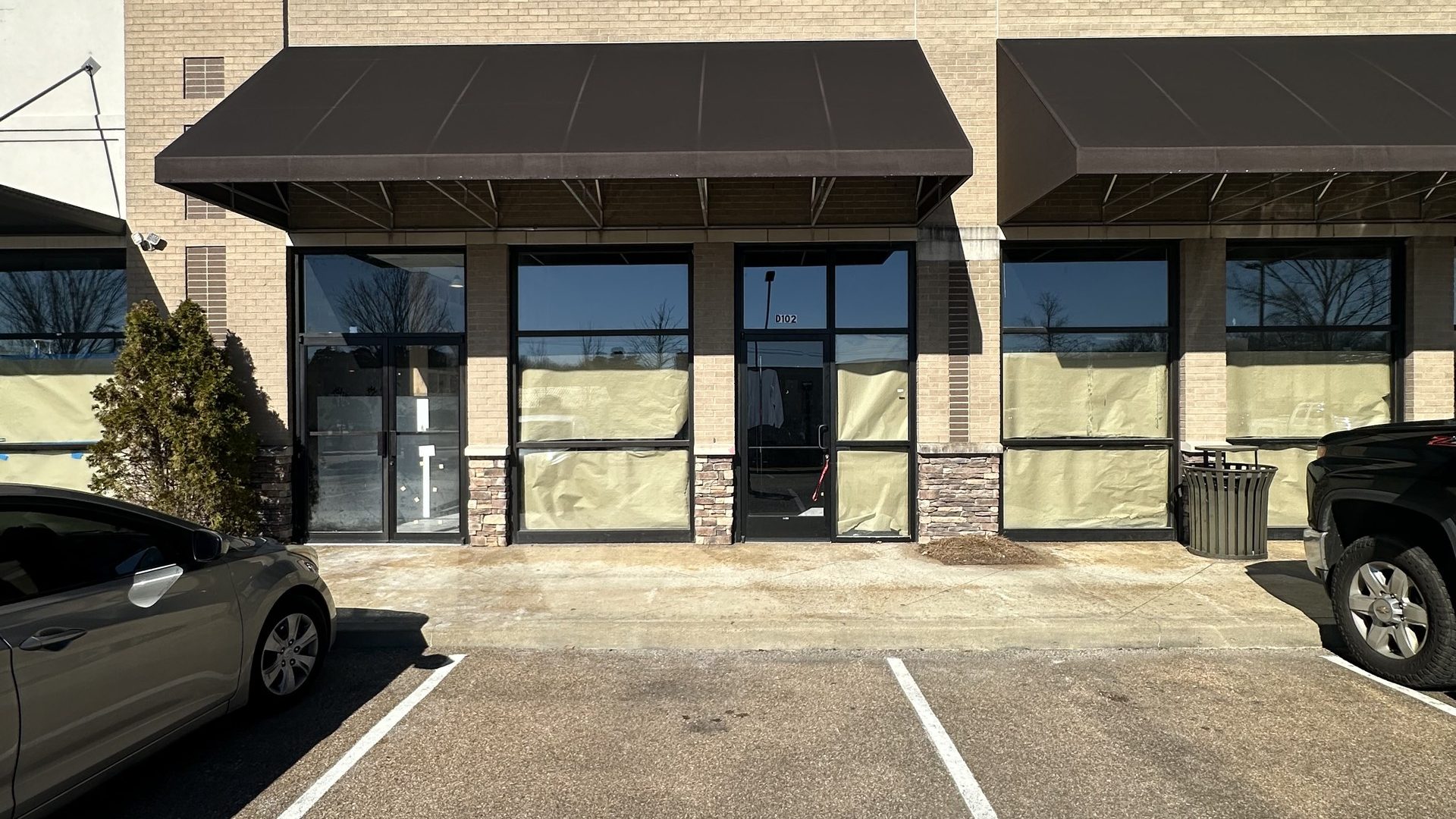 Brick strip center storefront with brown awnings and papered windows before buildout