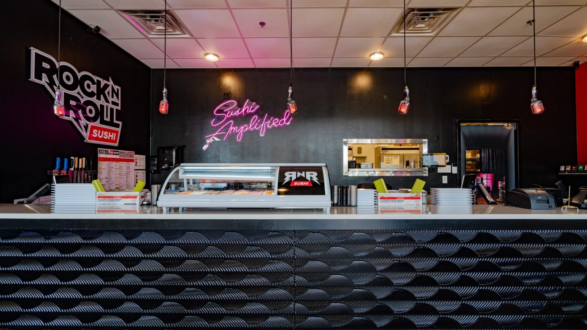 Sushi counter interior of Rock N Roll Sushi with neon sign and pendant lights